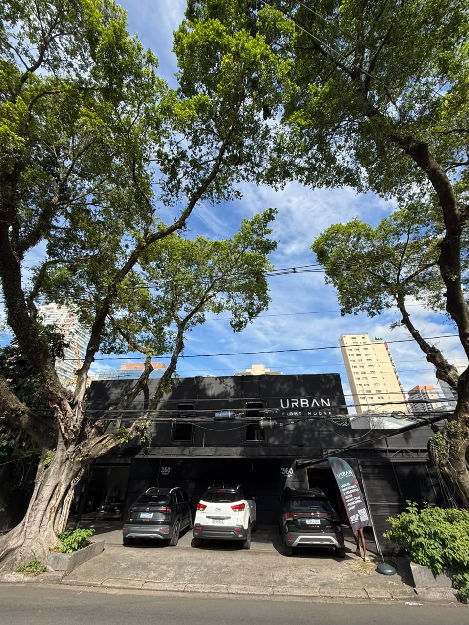 Fachada da Urban Fight House Vila Olímpia, na Rua Ribeirão Claro, em prédio preto entre árvores
