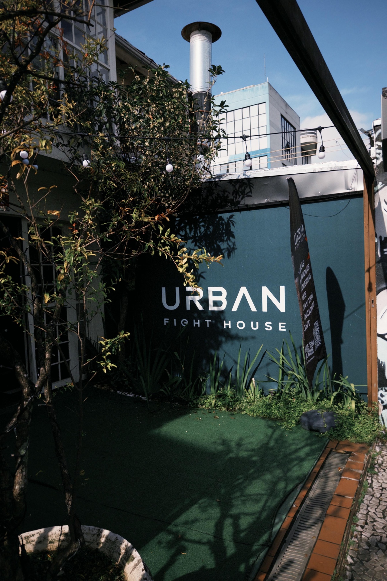 Fachada da Urban Fight House Vila Madalena com jardim e logo na parede