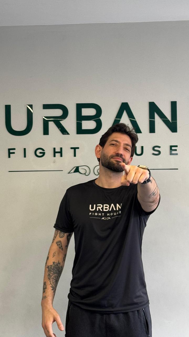 Nick Farinelli, founder e head coach da Urban Fight House, em pé na frente do logo da academia