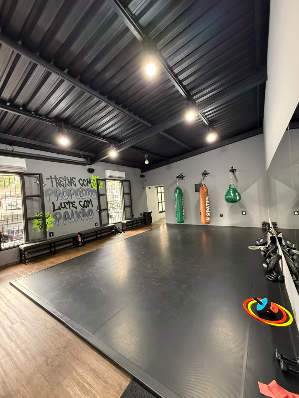 Sala de treino da Vila Olímpia com grafite treine com propósito, lute com paixão e sacos de pancada